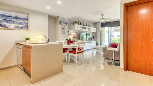 Una cocina moderna con una isla central, armarios blancos y un comedor con una silla roja.
