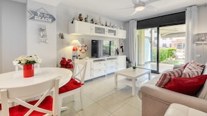 Una sala moderna con comedor, una cocina con televisor grande y puerta corrediza al exterior.