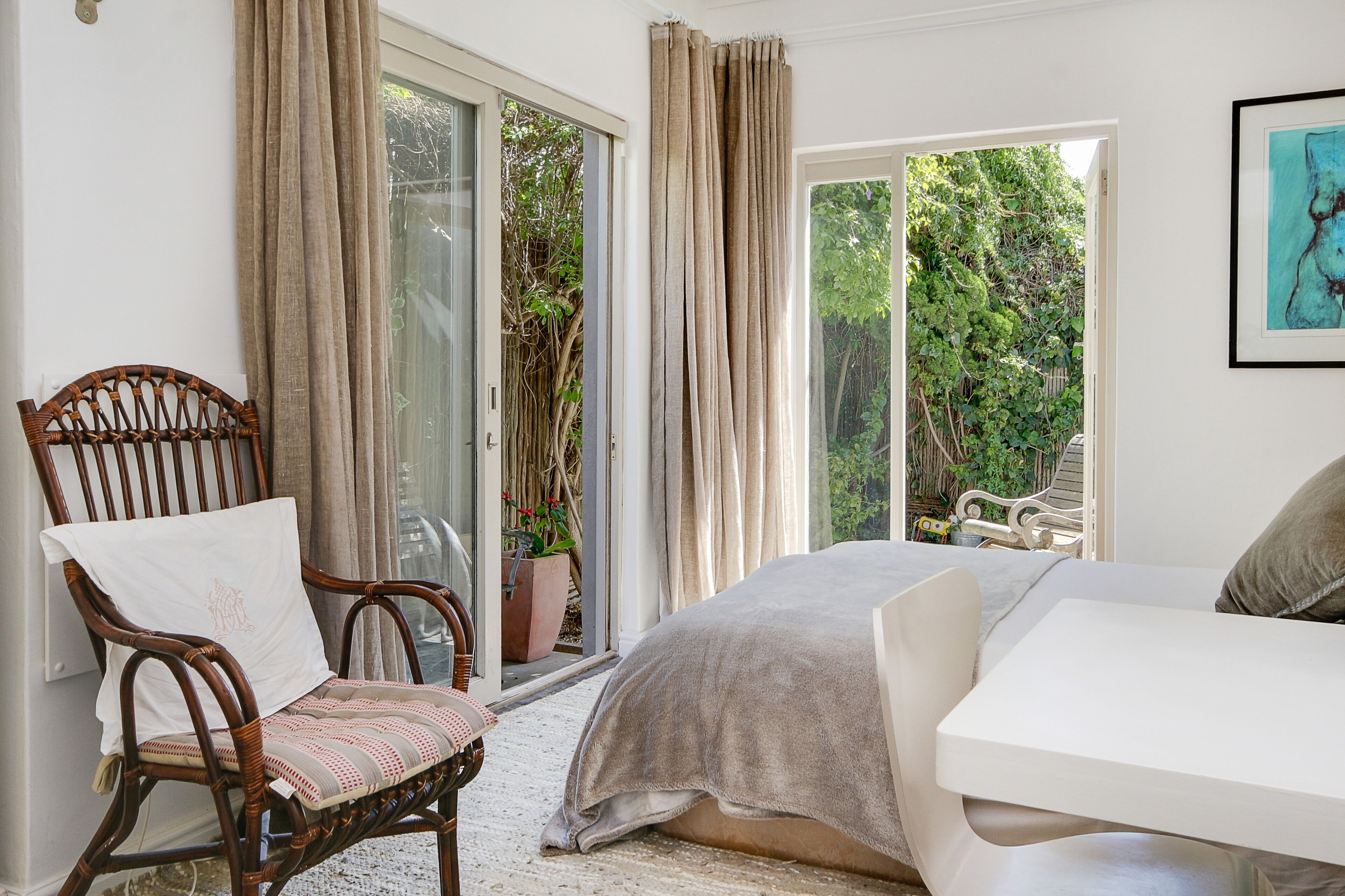 A bedroom with a bed, a chair, a table, and a view of a garden through a sliding door.