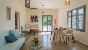 A modern living room with a sofa, a dining table with chairs, a glass coffee table, and a colorful abstract painting on the wall. - Villa with private pool and sea view located between Chania and Rethymnon, Lake Kournas (Patima)