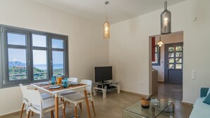A modern living room with a dining area, large windows, a flat-screen TV, and a cozy seating area. - Villa with private pool and sea view located between Chania and Rethymnon, Lake Kournas (Patima)