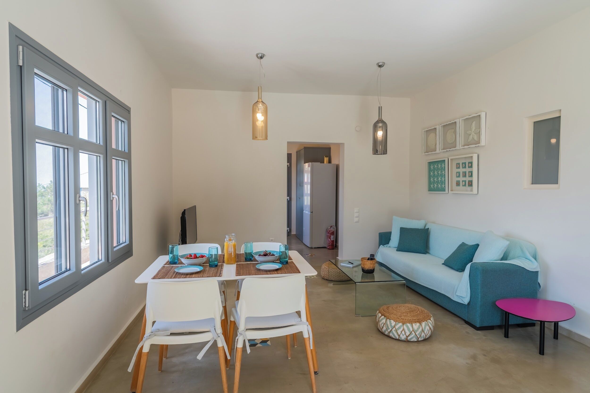 Una sala moderna con un sofá azul, una mesa de centro de vidrio y una zona de comedor con una mesa y sillas blancas.