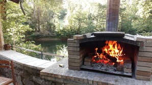 Una chimenea de ladrillo al aire libre con fuego encendido, rodeada de muros de piedra y vista a un lago.