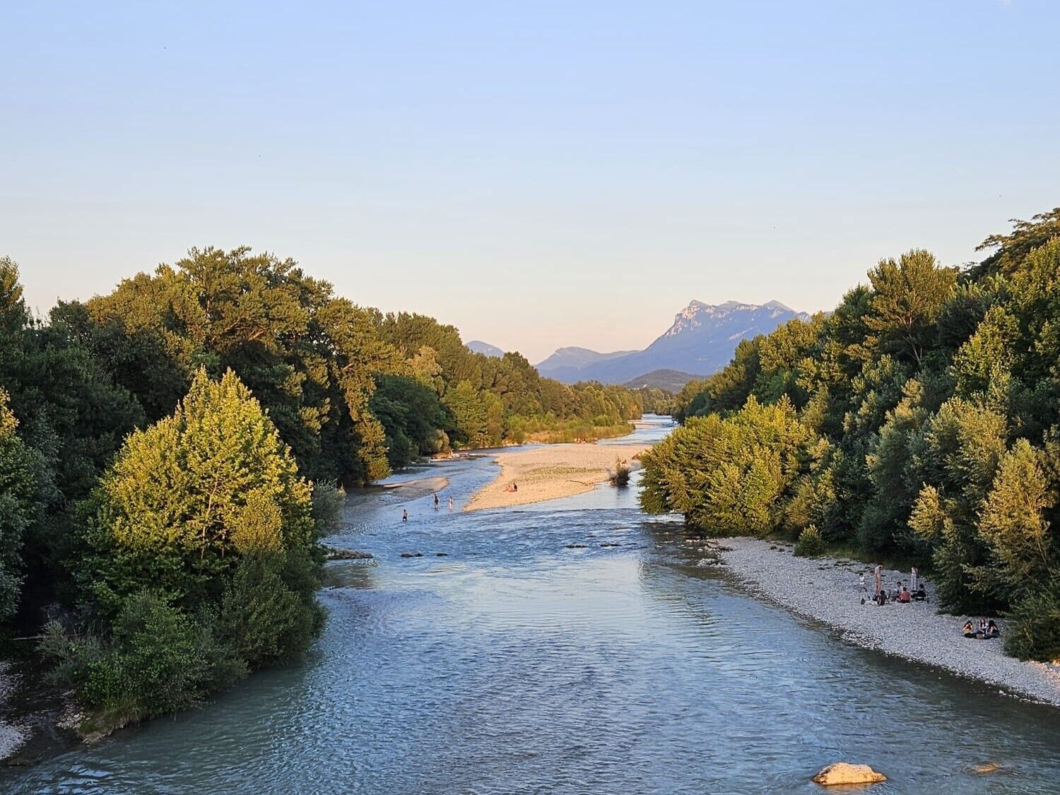 A river flanked by dense forests and mountains in the background.