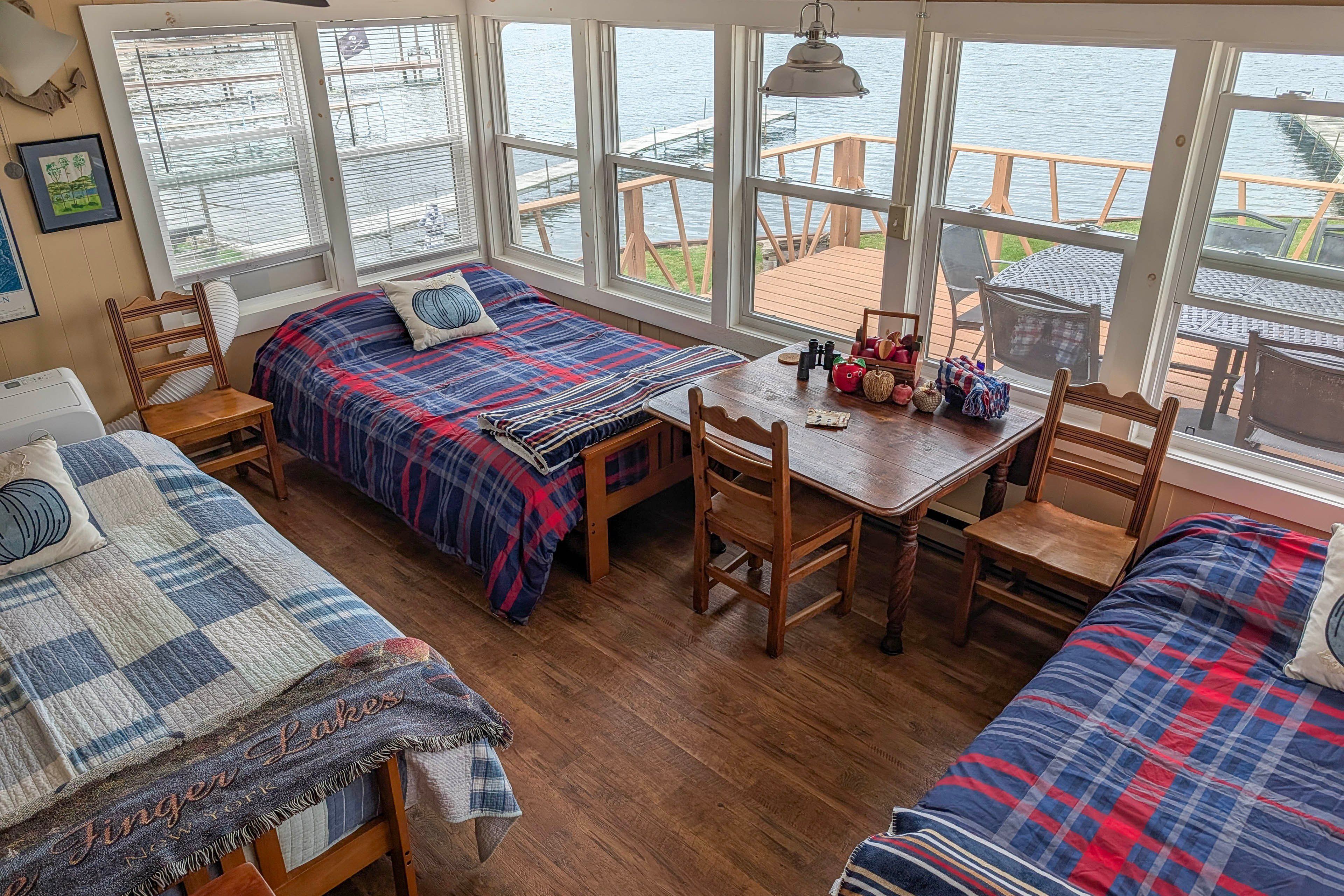 A cozy cabin with a large window overlooking a dock, wooden furniture, and a view of the water.
