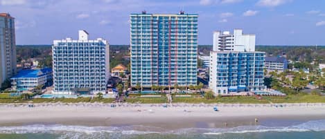 Un hotel frente a la playa con varios edificios altos, una playa de arena y vistas al océano.