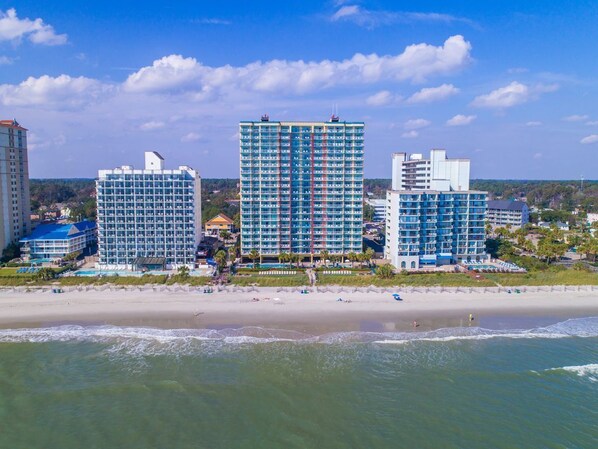 Un hotel frente a la playa con varios edificios altos, una playa de arena y vistas al océano.