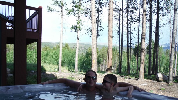 Zwei Personen entspannen in einer Badewanne mit Blick auf einen Wald.