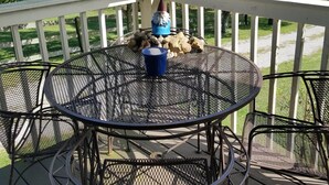 Une table ronde en métal, entourée de chaises, posée sur une terrasse en bois, ainsi qu’une statuette de gnome décorative et un récipient bleu.