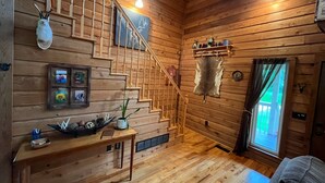 Un intérieur en bois avec un escalier, une étagère murale agrémentée d’objets décoratifs, un montage de photos encadrées et un élément en fourrure.