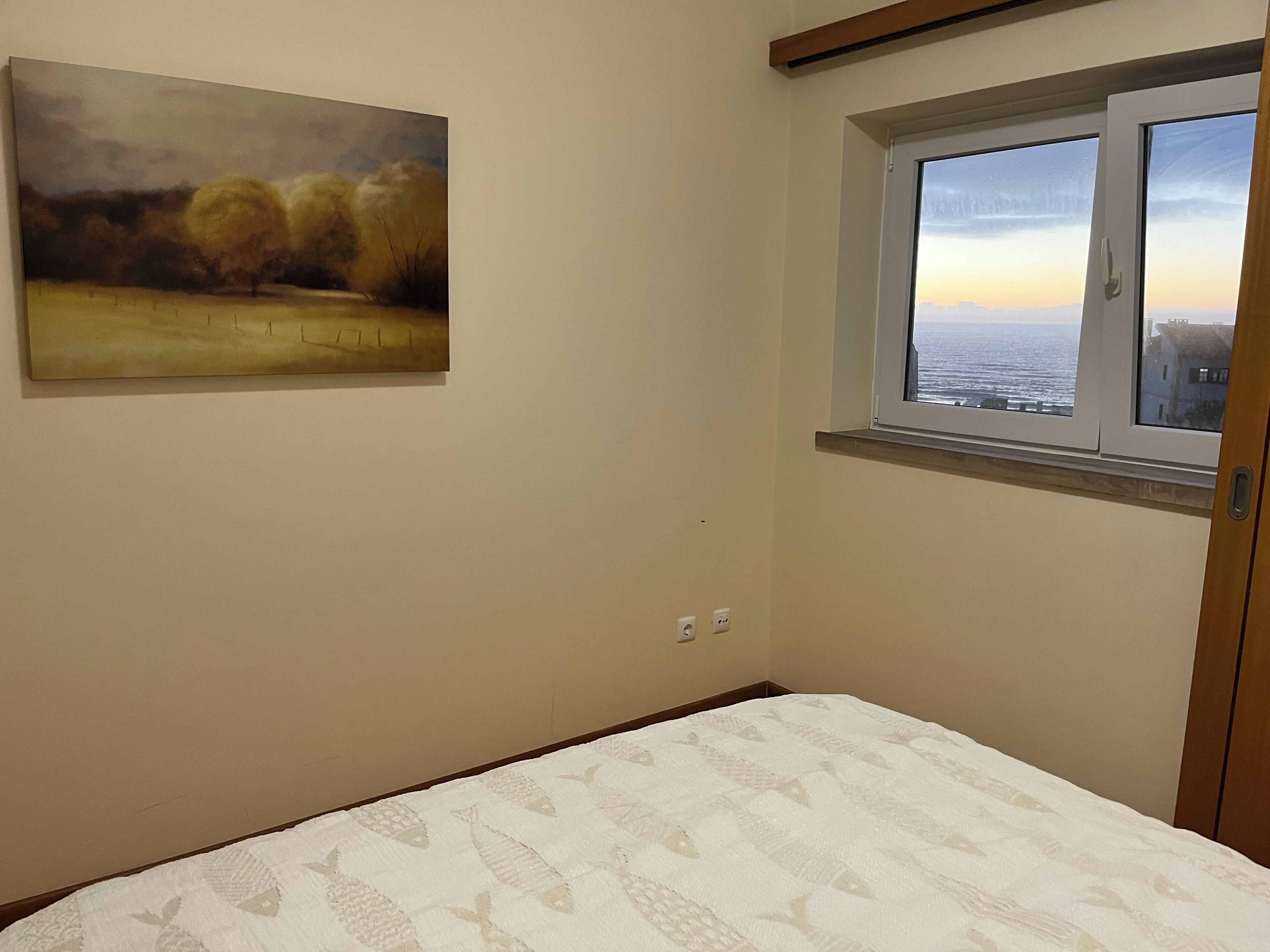 Ein Schlafzimmer mit Bett, Fenster mit Meerblick und einem Bild an der Wand.