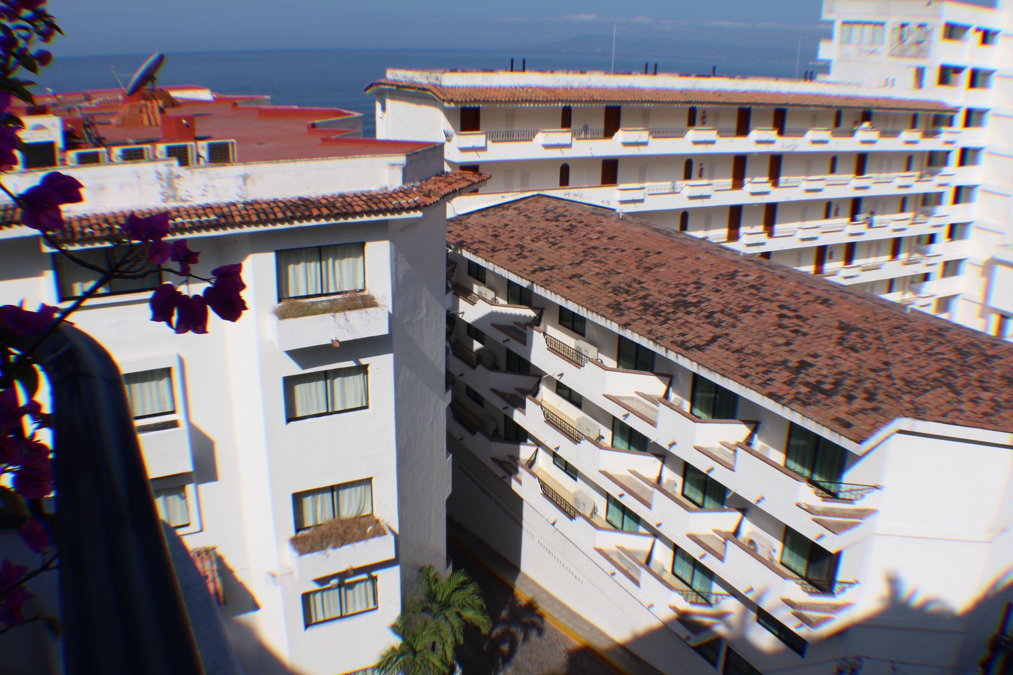 A multi-story hotel with balconies, a tiled roof, and a view of the sea.