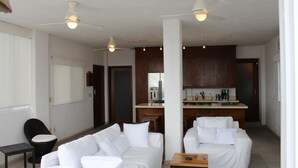 A modern living area with white sofas, a small table, and a ceiling fan. There is a kitchen area in the background with wooden cabinets and a coffee maker. - COOL 1 bedroom large condo with spa like bath.... enjoy!! (Col. Em. Zapata, Puerto Vallarta)