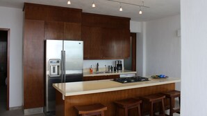 A modern kitchen with wooden cabinets, a stainless steel refrigerator, a coffee maker, and a bar area with stools. - COOL 1 bedroom large condo with spa like bath.... enjoy!! (Col. Em. Zapata, Puerto Vallarta)