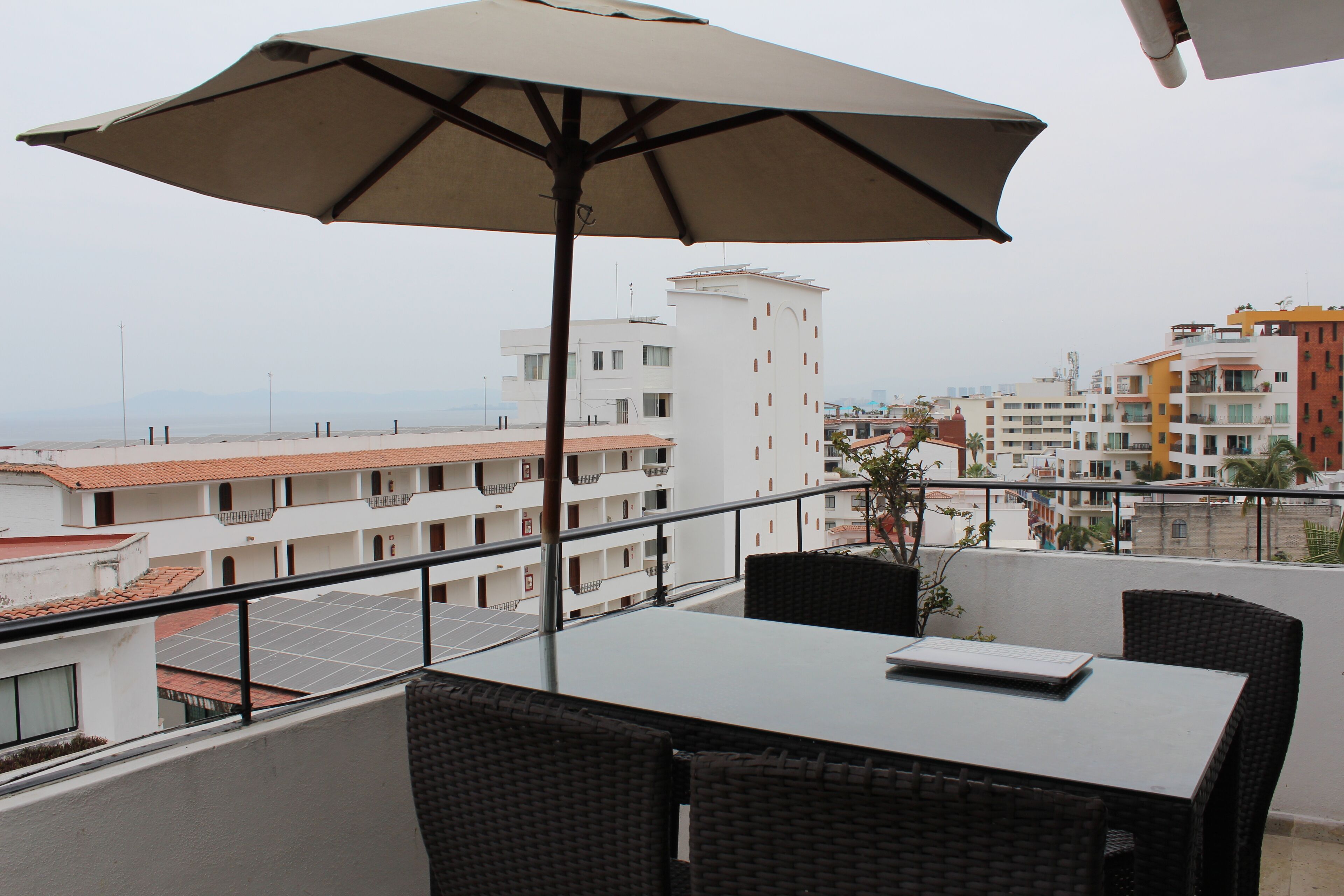 A balcony with a table and chairs, an umbrella, and a view of buildings in the background.