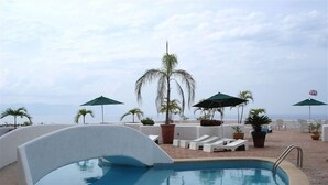 A pool area with lounge chairs and umbrellas, surrounded by palm trees and a view of the ocean. - COOL 1 bedroom large condo with spa like bath.... enjoy!! (Col. Em. Zapata, Puerto Vallarta)