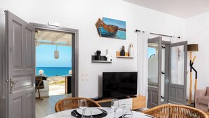 Un espacio habitable de concepto abierto con vista al mar, un televisor, muebles de mimbre y una zona de comedor.