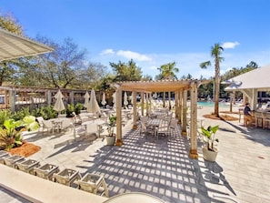 An outdoor patio area with tables and chairs, a pergola, and a pool in the background. - Carriage House-2 bikes-300 Yards to Frog Pool! (Santa Rosa Beach)