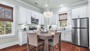 A kitchen with white cabinets, a wooden dining table, a chandelier, and stainless steel appliances.