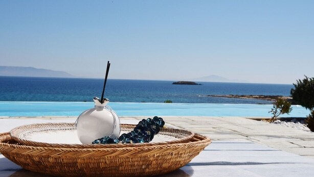 A wicker basket with a white vase and grapes on a terrace with a pool and ocean view. - Villa-waterfront, infinity pool-splendid views-luxurious amenities  (PAROS)