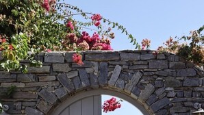An arched stone entrance with a wooden door leading to a paved path. - Villa-waterfront, infinity pool-splendid views-luxurious amenities  (PAROS)