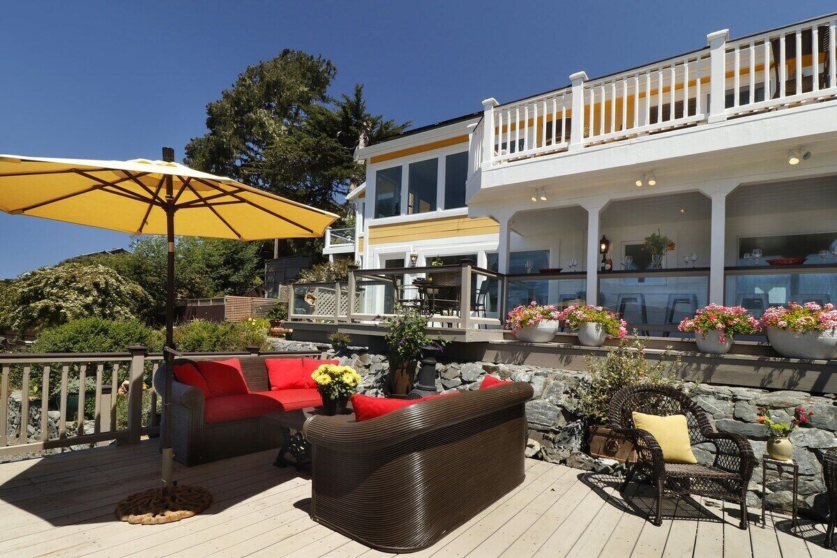 A deck with wicker furniture, a yellow umbrella, and potted plants.