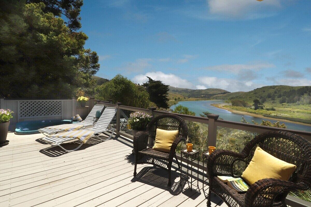 Terraza con sillones de descanso y una silla de mimbre, con vistas a un río y colinas.