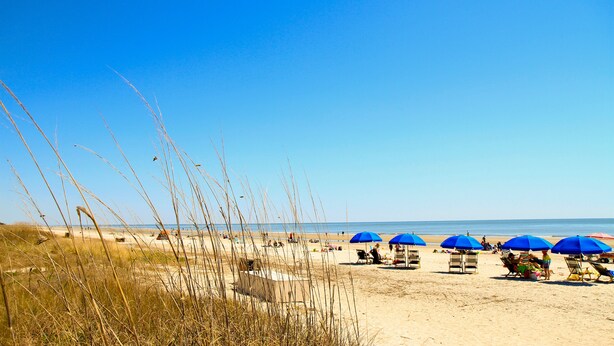 Ein Strand mit blauen Sonnenschirmen und entspannten Menschen.