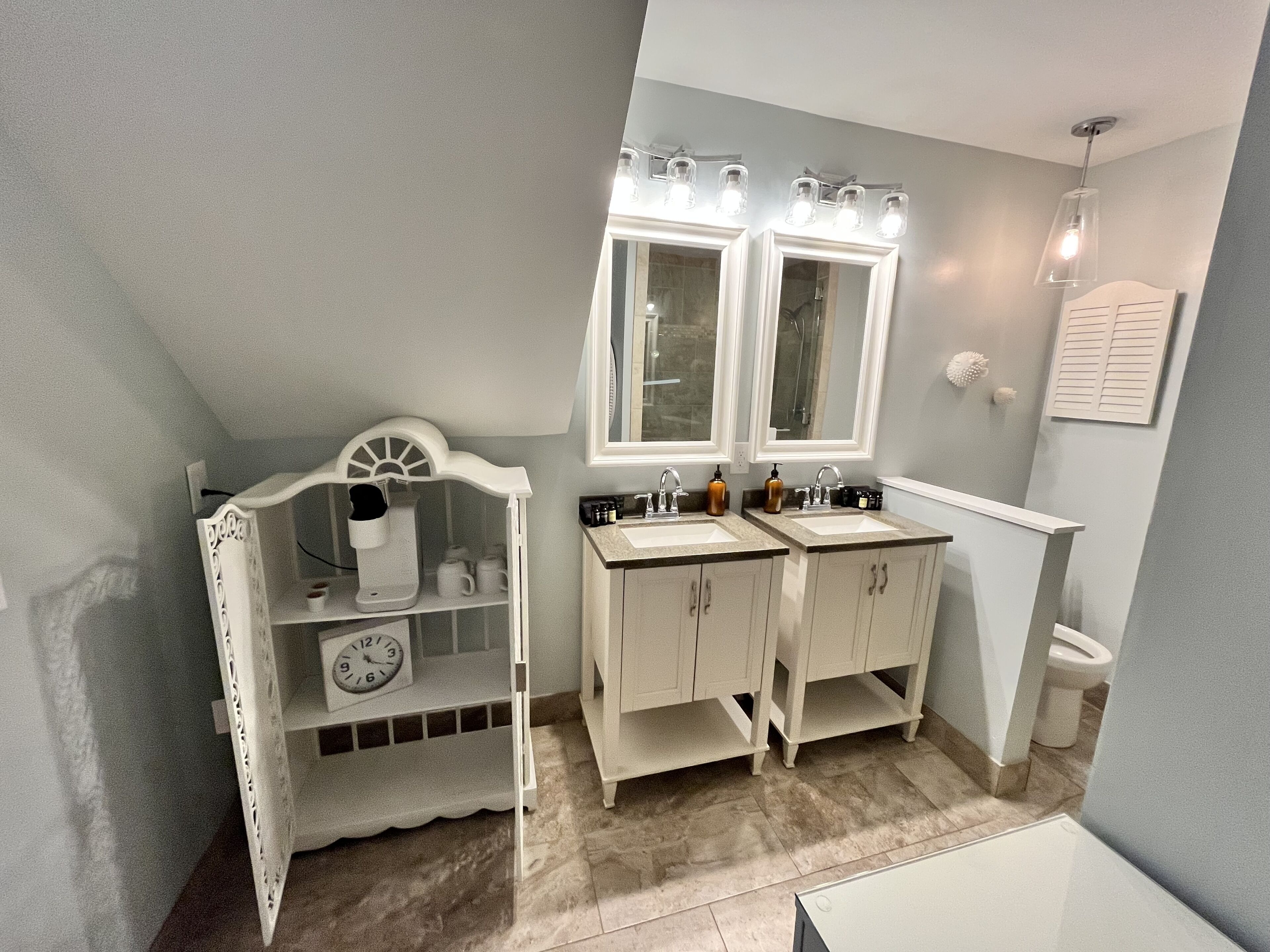 Een badkamer met twee wasbakken, een wastafelmeubel met een klok, en een douchehoek.