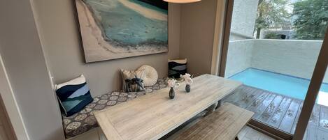A dining area with a wooden bench, a table with decorative vases, and a large painting of a wave on the wall.