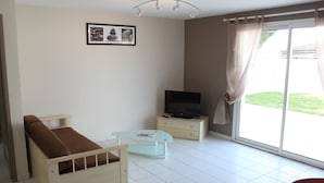 Un dormitorio con cama, televisor, mesa de vidrio y ventana con cortinas.
