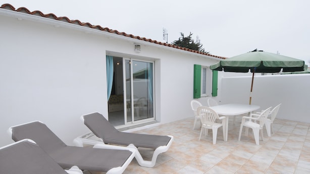 Un patio con sillones de descanso, una mesa y sillas, y una sombrilla verde.