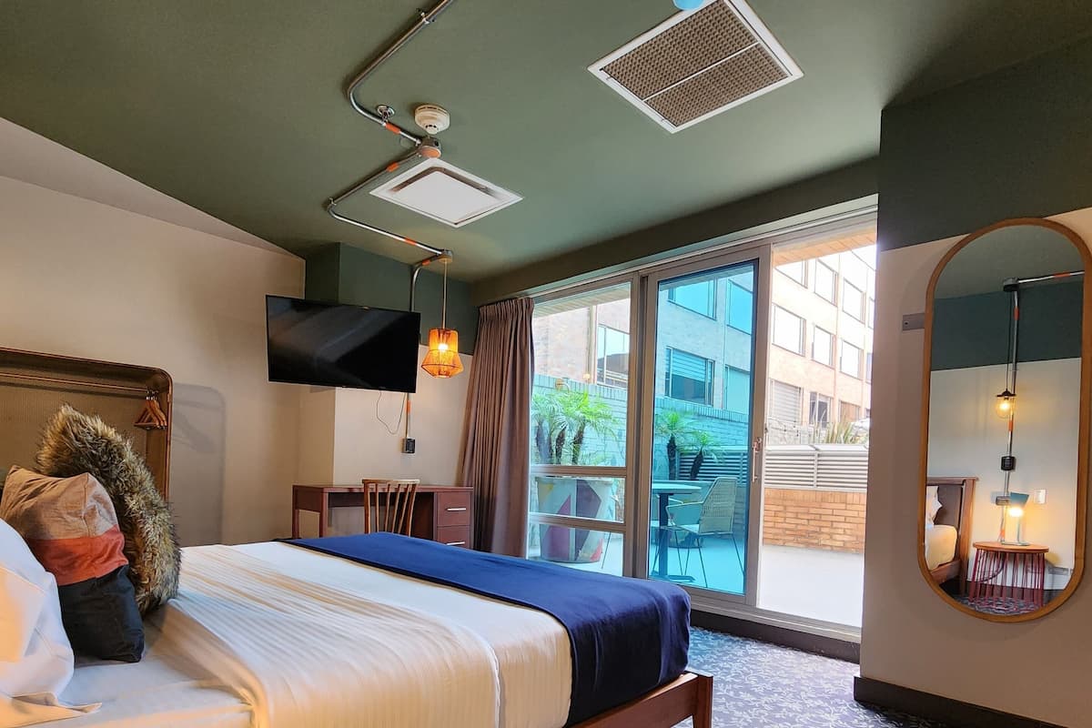Et moderne hotelværelse med en stor seng, et fladskærms-tv, en ventilator i loftet og et stort vindue med udsigt over byen.