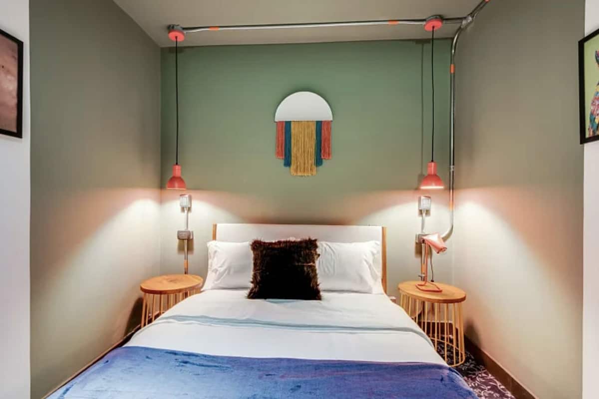 Et soveværelse med seng, to sengeborde, en hængende lampe og en rund dekoration på væggen.