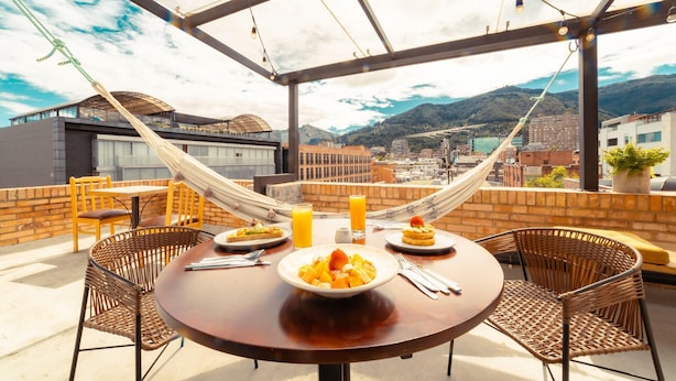 A rooftop terrace with a dining table, wicker chairs, a hammock, and a city view. - Socialtel Parque 93 Bogota (Bogotá)