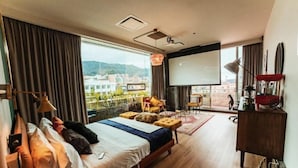 A modern hotel room with a large bed, a desk with a computer, a projector screen, and a view of the city through large windows. - Socialtel Parque 93 Bogota (Bogotá)