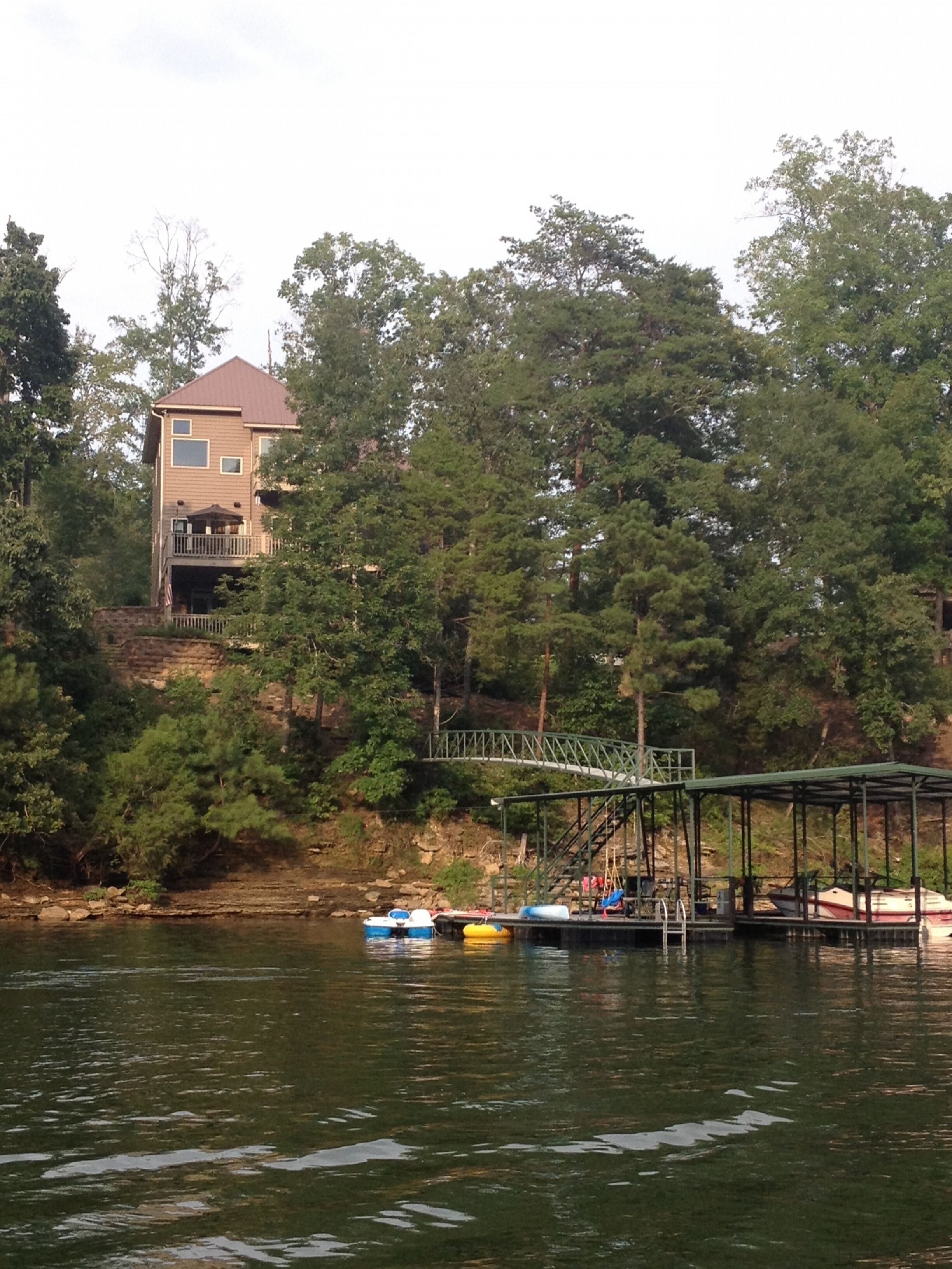 A house with a balcony, surrounded by dense trees and a dock with boats.