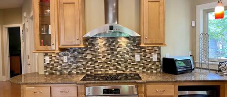 A kitchen with wooden cabinets, a stainless steel range hood, a microwave, and a granite countertop.