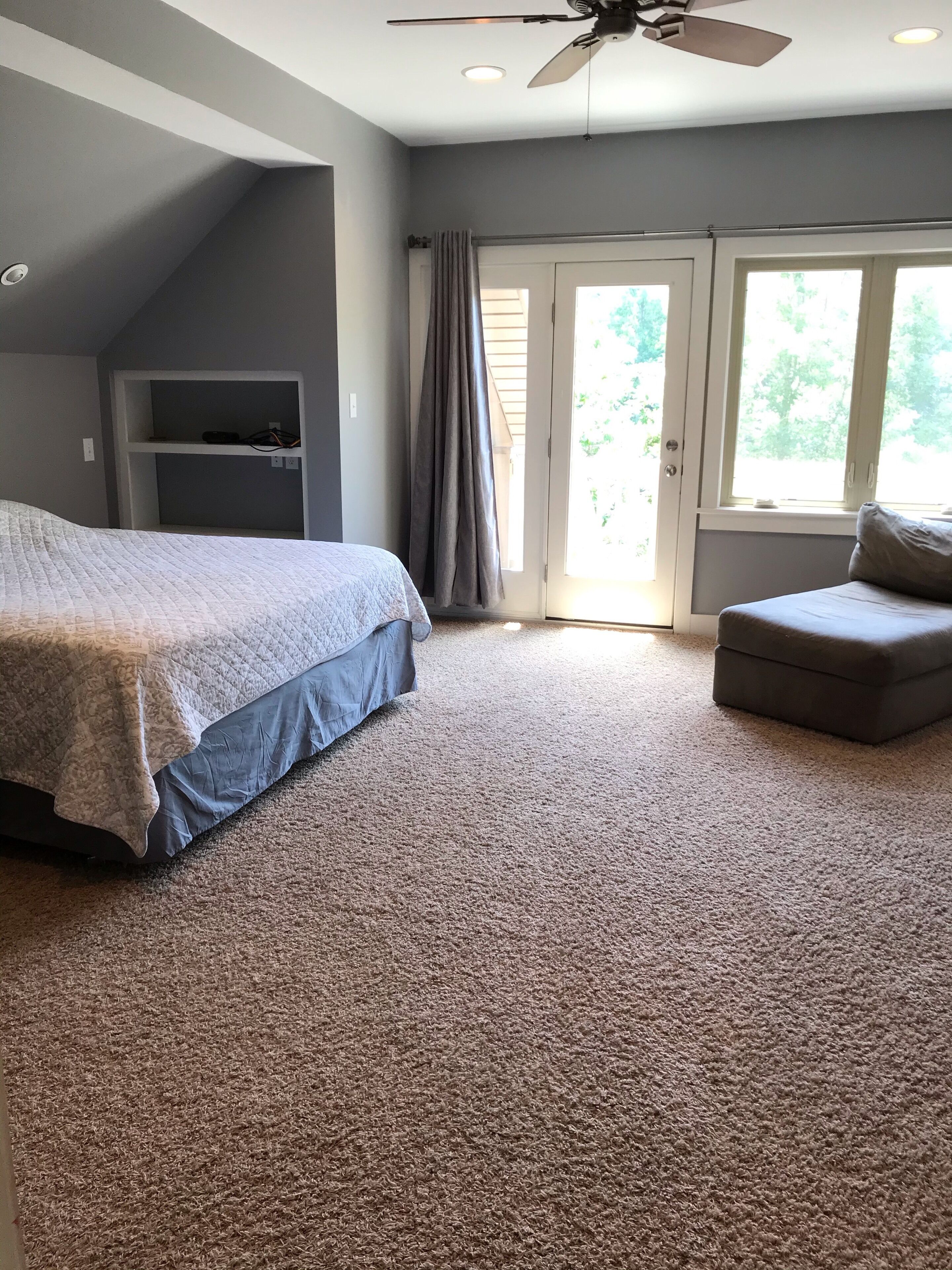 Ein Schlafzimmer mit Bett, Stuhl, Deckenventilator, Fenster und Tür.