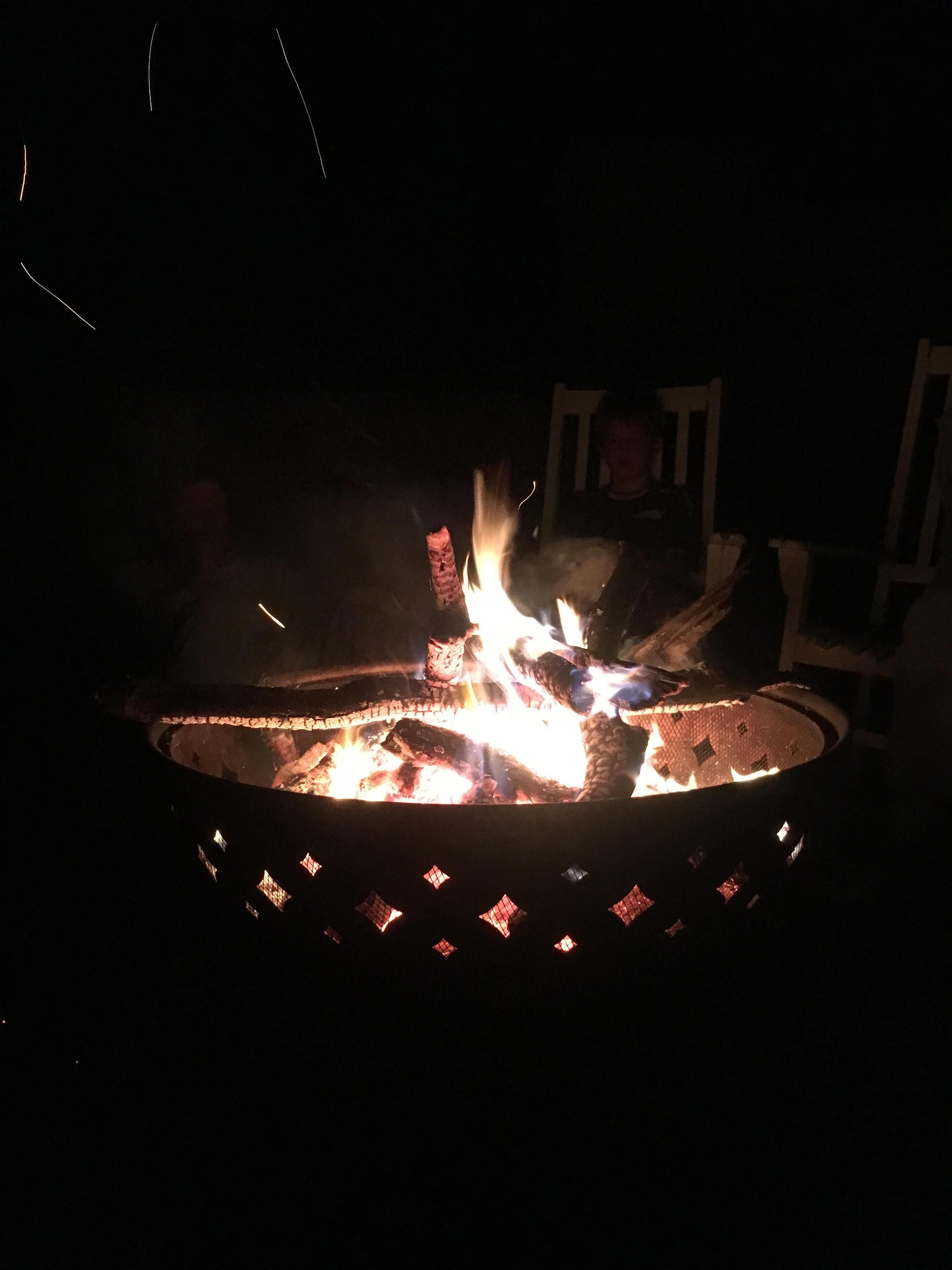A fire pit with logs burning, surrounded by a metal rim with diamond-shaped cutouts.