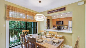 Zona pranzo con tavolo in legno apparecchiato per quattro, cucina dotata di elettrodomestici moderni e vista sul verde dalla finestra.