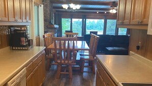 Una cocina con armarios de madera, una mesa de comedor con sillas, una cafetera y vistas al exterior a través de amplios ventanales.