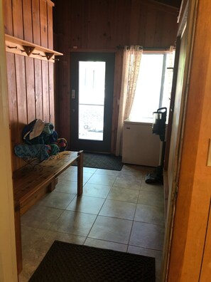 A wooden interior with a bench, a door leading outside, and a vacuum cleaner.