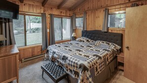 Un dormitorio de cabaña de madera con una cama grande, un banco y un televisor.