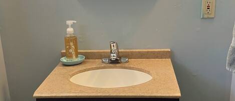 A bathroom with a sink, a mirror, a soap dispenser, and a towel rack.