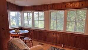 Une pièce chaleureuse aux murs en bois et aux grandes fenêtres, avec une table ronde entourée de chaises et un fauteuil confortable.