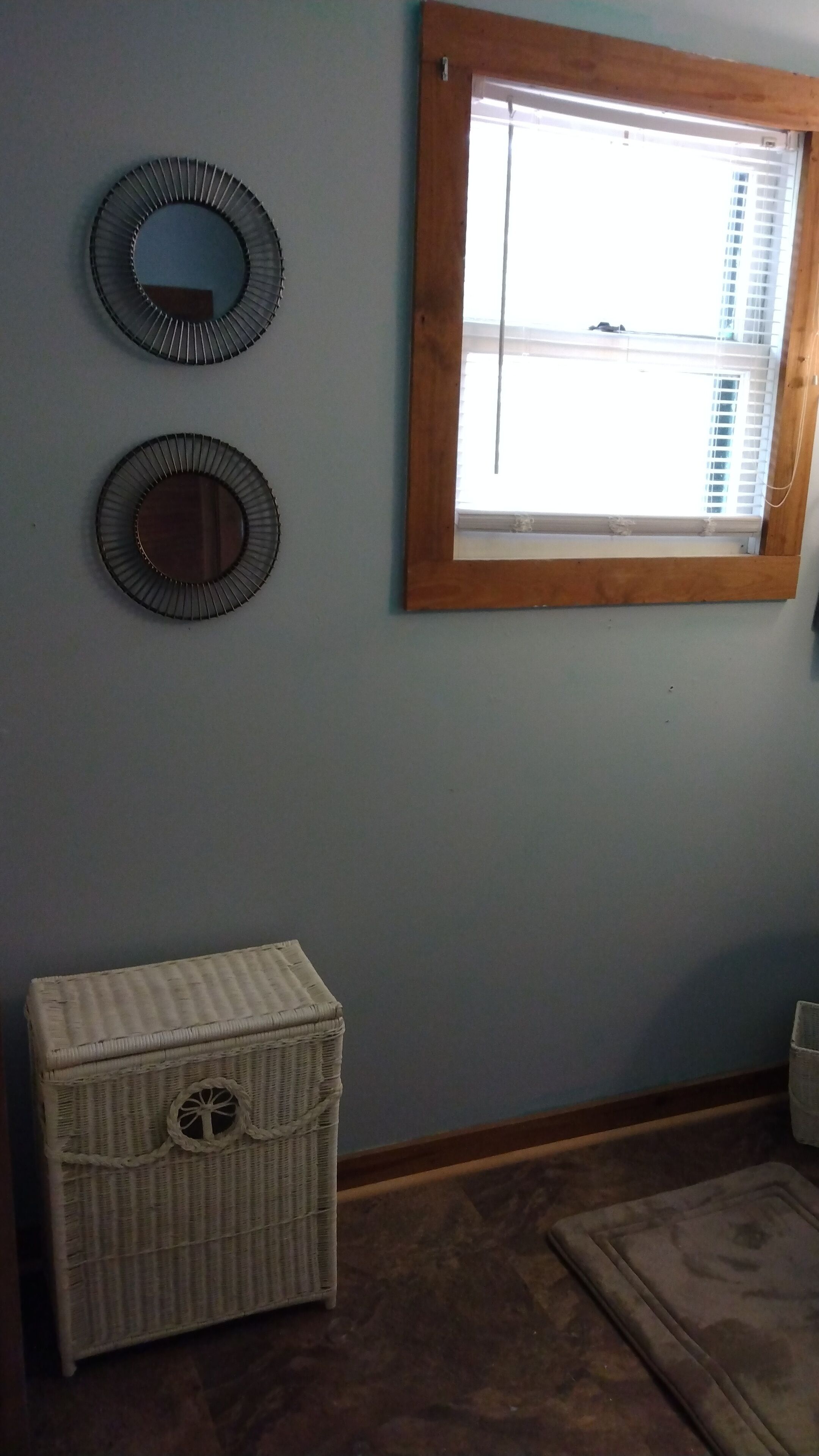 A room with a window, two wall-mounted mirrors, and a wicker chest of drawers.