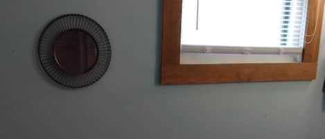 A room with a window, two wall-mounted mirrors, and a wicker chest of drawers.