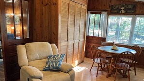 Une pièce chaleureuse avec un fauteuil beige, une table à manger entourée de chaises en bois et une vue sur l’extérieur par une fenêtre.