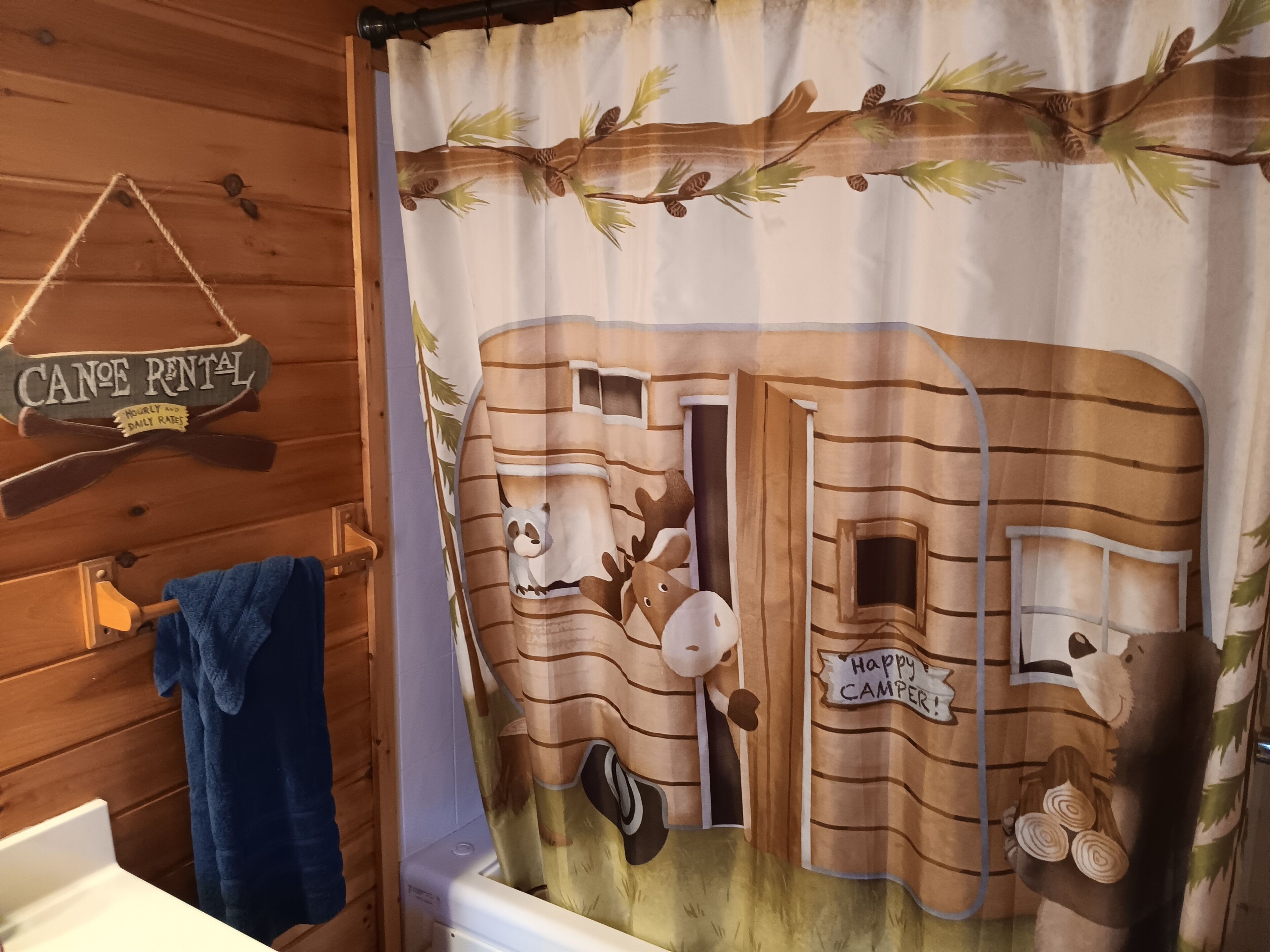Un baño con cortina de ducha de estilo rústico de cabaña, un perchero y un letrero que indica las tarifas de alquiler de canoas.